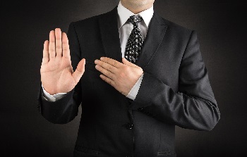 man in dark suit raising right hand with left hand on chest